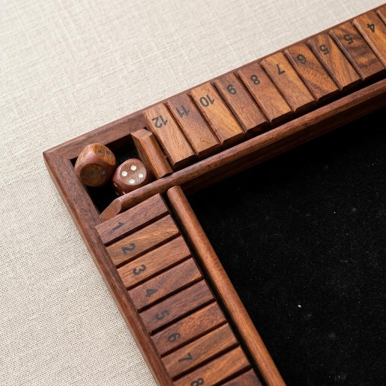 May include: A wooden shut-the-box game with a dark finish. The game features numbered wooden tiles and two dice. The playing surface is black. The numbers are printed in a clear, easy-to-read font. The game is designed for multiple players.