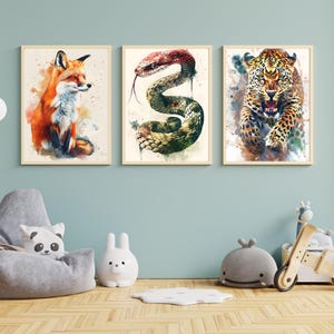 May include: Three framed watercolor animal prints. The prints feature a fox, a snake, and a leopard. The fox is orange and white. The snake is green and brown. The leopard is tan with black spots. The frames are light brown.