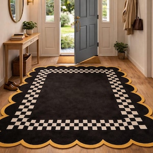 May include: A black rectangular rug with a scalloped yellow border and a white and black checkered pattern. The rug is placed in a doorway with a wooden floor. The door is open, revealing a view of the outside.