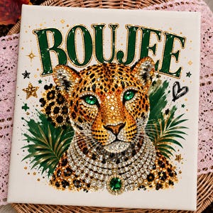 May include: A square canvas print featuring a leopard with bright green eyes, wearing a multi-layered rhinestone necklace with a central green gem. The word BOUJEE is printed in large green letters above the leopard, surrounded by gold stars and palm leaves.
