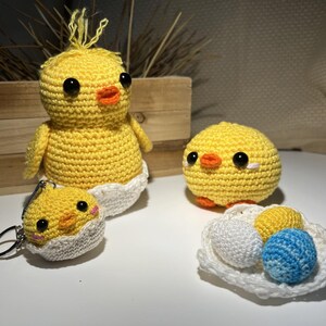 May include: A collection of handmade crochet Easter decorations. The set includes a large yellow chick emerging from a white egg, a smaller chick, a keychain chick, and a plate of crochet eggs in white, yellow, and blue.