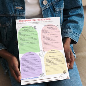 Op de afbeelding: Een gedrukt menu met de titel "ADHD Dopamine Menu: Fuel Your Focus" wordt vastgehouden door een persoon die een spijkerjasje draagt. Het menu bevat secties voor voorgerechten, hoofdgerechten, bijgerechten en desserts, met verschillende activiteiten.