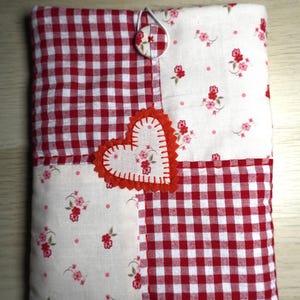 Puede incluir: Funda de tela acolchada con diseño de patchwork. Presenta cuadrados de cuadros rojos y blancos y secciones con estampado floral. Un corazón rojo está cosido en la parte delantera. Cierre con botón y lazo.