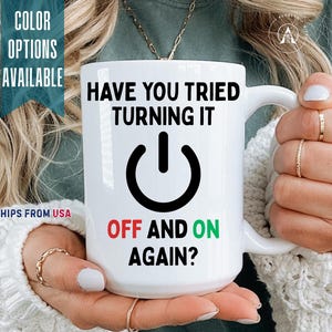 May include: A white ceramic mug featuring the black text HAVE YOU TRIED TURNING IT, a black power symbol icon, and the text OFF AND ON AGAIN? with the word OFF in red and the word ON in green. The mug has a curved handle on the right side.
