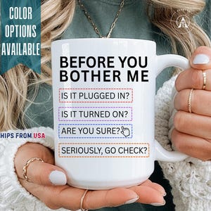May include: A white ceramic mug featuring black text that reads: BEFORE YOU BOTHER ME, IS IT PLUGGED IN?, IS IT TURNED ON?, ARE YOU SURE?, SERIOUSLY, GO CHECK?. The text is organized in boxes with red, purple, blue, and orange dashed borders.