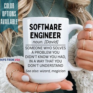 May include: A white ceramic mug featuring black printed text that reads: SOFTWARE ENGINEER noun. [David] SOMEONE WHO SOLVES A PROBLEM YOU DIDN'T KNOW YOU HAD, IN A WAY THAT YOU DON'T UNDERSTAND See also: wizard, magician. The mug has a smooth handle.