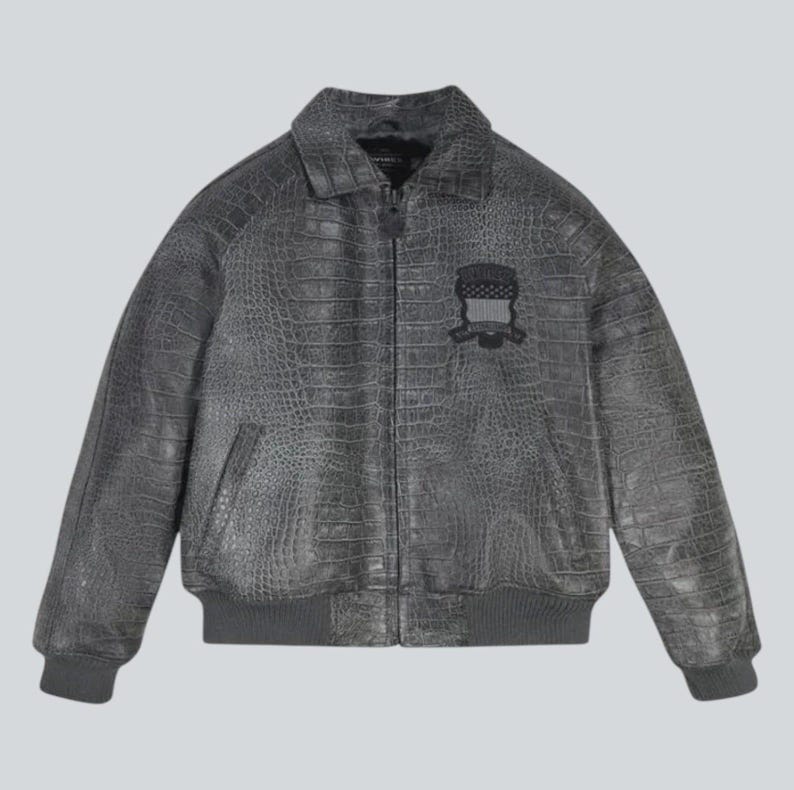 Puede incluir: Chaqueta de cuero gris con textura de cocodrilo. Cuenta con cuello, cierre de cremallera y parche en el pecho. Dobladillo y pu&ntilde;os de canal&eacute;. Prenda de abrigo elegante.