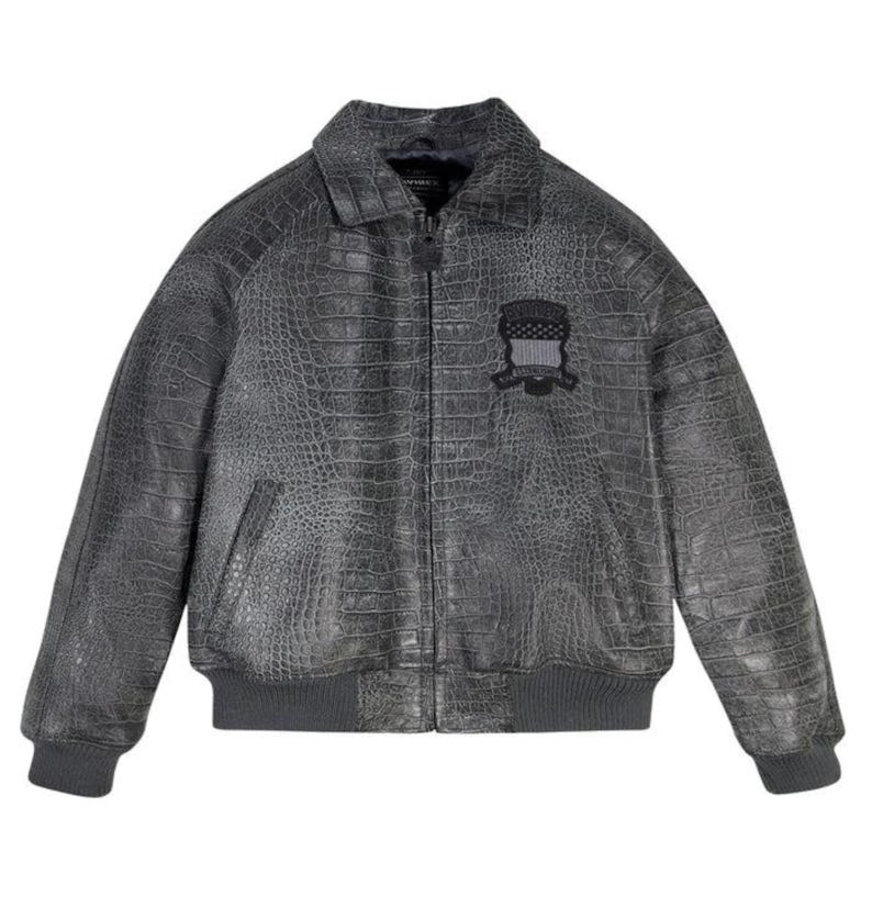 May include: A gray, faux-leather bomber jacket with a crocodile skin texture. The jacket features a collar, a zipper closure, and a small patch on the chest. The cuffs and hem are ribbed.