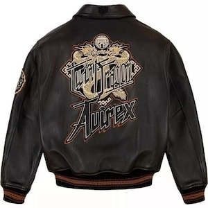 May include: Black leather jacket with a classic bomber silhouette. Features a large embroidered design on the back with a dragon motif and the text "Tokyo Dragon" and "Avirex" in gold and black. The jacket has a ribbed collar and cuffs.