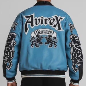 May include: A light blue leather jacket with black and white accents. The back features the word "Avirex" above "New York" and two lion graphics. Black lion graphics are on the sleeves.
