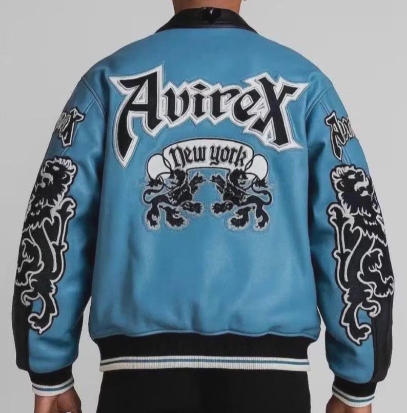 May include: A light blue leather jacket with black and white accents. The back features the word "Avirex" above "New York" and two lion graphics. Black lion graphics are on the sleeves.