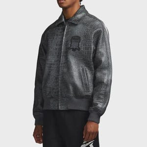 Puede incluir: Chaqueta bomber gris con textura de piel de cocodrilo. La chaqueta tiene cuello, cierre de cremallera y un peque&ntilde;o emblema en el pecho. Tiene pu&ntilde;os y dobladillo de canal&eacute;. El modelo lleva pantalones negros.