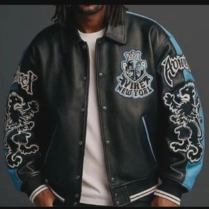 May include: Black leather varsity jacket with blue accents on the sleeves and embroidered lion graphics. Features the text "Virey New York" and a crest design on the chest. The jacket has a button-up front and white striped cuffs.