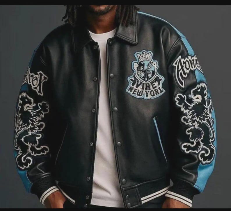 May include: Black leather varsity jacket with blue accents on the sleeves and embroidered lion graphics. Features the text "Virey New York" and a crest design on the chest. The jacket has a button-up front and white striped cuffs.