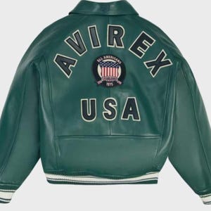 May include: Green leather jacket with white and black striped cuffs and hem. The back of the jacket features the word "AVIREX" in white block letters, above a patch with a red, white, and blue design and the word "USA" in white block letters.