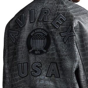 May include: A dark gray jacket with a crocodile skin texture. The back of the jacket features the words "AIR," "REX," and "USA" in raised, dark gray lettering. A circular patch with "ALL AMERICANS" and "ESTABLISHED 1975" is also visible.