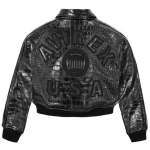 May include: Black leather jacket with a crocodile skin texture. The jacket features the brand name "AVIREX" and "USA" in raised lettering on the back. The jacket has a ribbed collar, cuffs, and hem.