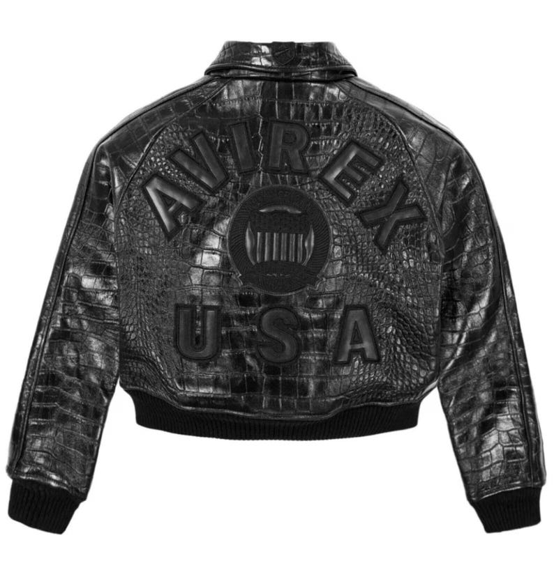 May include: Black leather jacket with a crocodile skin texture. The jacket features the brand name "AVIREX" and "USA" in raised lettering on the back. The jacket has a ribbed collar, cuffs, and hem.