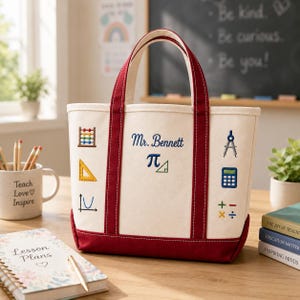 May include: A cream-colored canvas tote bag with dark red handles and base. The front features embroidered math-themed icons including an abacus, triangle, parabola, compass, calculator, and symbols. It is personalized with the text Mr. Bennett and pi.