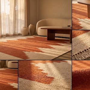May include: A rectangular area rug featuring a geometric pattern in burnt orange and cream. The rug has a textured, woven surface with short fringe detailing along the edges, showcasing a repeating jagged or stepped design across the fabric.