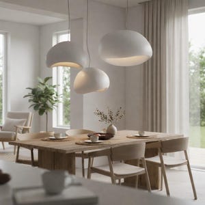 Peut inclure: Trois lampes suspendues blanches de forme organique sont suspendues au-dessus d'une table à manger en bois. La table est dressée avec des sets de table, des tasses et un vase de verdure. La pièce a une palette de couleurs neutres.