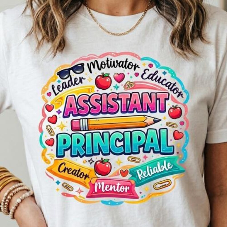 May include: White t-shirt with a colorful graphic design. The design features the words "Assistant Principal" in large letters, surrounded by other words like "Leader," "Educator," and "Mentor." A pencil and apple are also included.