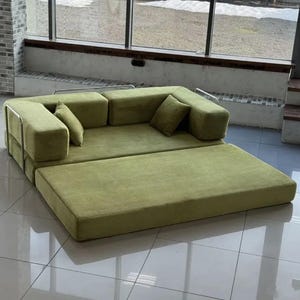 Op de afbeelding: Een modulaire, olijfgroene bank met een modern design. De bank heeft een laag profiel, met een grote rechthoekige basis en verschillende vierkante kussens. Twee bijpassende sierkussens zijn inbegrepen. De bank heeft een metalen frame aan de zijkanten.