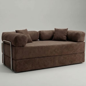 Könnte beinhalten: Ein braunes Cord-Sofa mit rechteckiger Basis und mehreren passenden Kissen. Das Sofa hat ein Metallgestell und ein minimalistisches Design. Die Kissen haben verschiedene Formen, darunter zylindrisch und quadratisch.