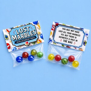 Puede incluir: Dos bolsas transparentes de canicas sobre un fondo azul. Una bolsa tiene una etiqueta que dice "LOST MARBLES REPLACEMENT PACK". La otra bolsa tiene una etiqueta que dice "YOU MAY NOT HAVE LOST ALL YOUR MARBLES YET, BUT THERE IS DEFINITELY A HOLE IN THE BAG".