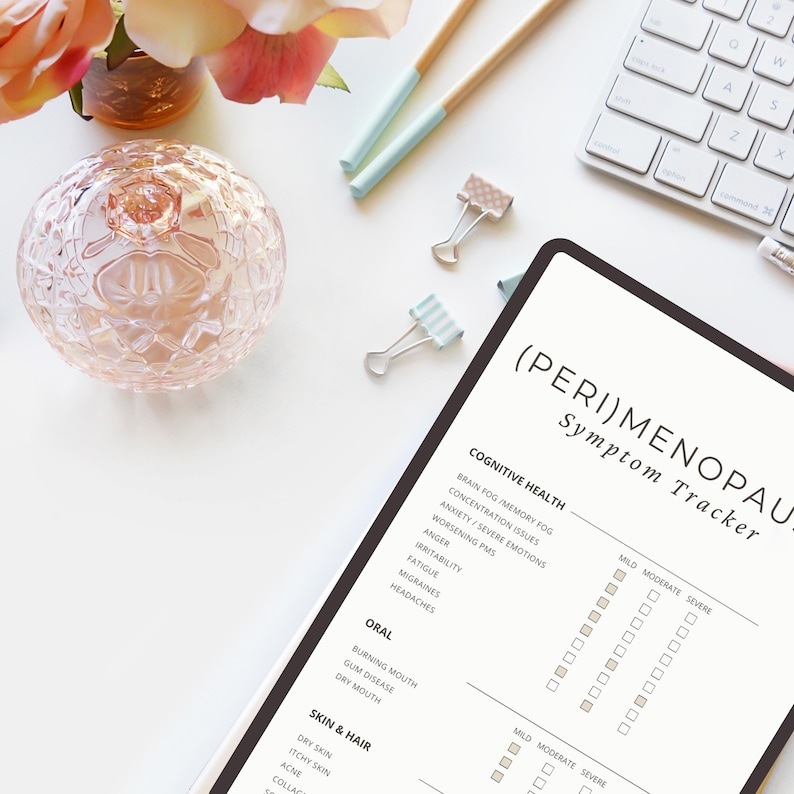 May include: A flat lay featuring a digital tablet with the text "(PERI)MENOPAUSE Symptom Tracker", a decorative glass sphere, stationery, and a keyboard. The tracker lists symptoms like brain fog, anxiety, and fatigue.