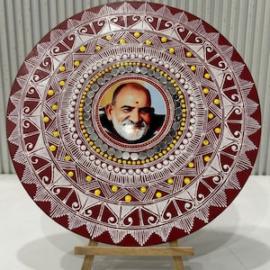 May include: A round, maroon decorative plate with a central portrait, surrounded by intricate white and yellow geometric patterns. The plate is displayed on a small wooden easel, showcasing its detailed design and craftsmanship.