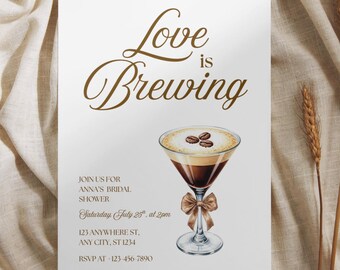 May include: A white rectangular invitation card featuring the brown text Love is Brewing at the top. Below is an illustration of a martini glass filled with dark coffee and foam topped with three coffee beans, adorned with a brown ribbon bow.