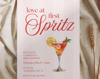 May include: A rectangular invitation card with a light pink striped background featuring the red text love at first Spritz. Below, a watercolor illustration of a cocktail in a glass with a lemon slice and berries, followed by event details for Charlotte's bridal shower on Saturday, July 25th at 2pm at 123 Any St, Anywhere City, ST, with an RSVP number.