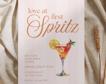 May include: A rectangular invitation card with a light pink striped background featuring the text love at first Spritz and details for Anna's bridal shower. A watercolor illustration of a cocktail in a glass with a lemon slice is included.