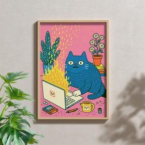 May include: A framed art print featuring a blue cat sitting at a laptop that is engulfed in yellow flames. The background is pink, with a green potted plant, a flower pot, a small yellow mug, a book, and a pen scattered on the surface.