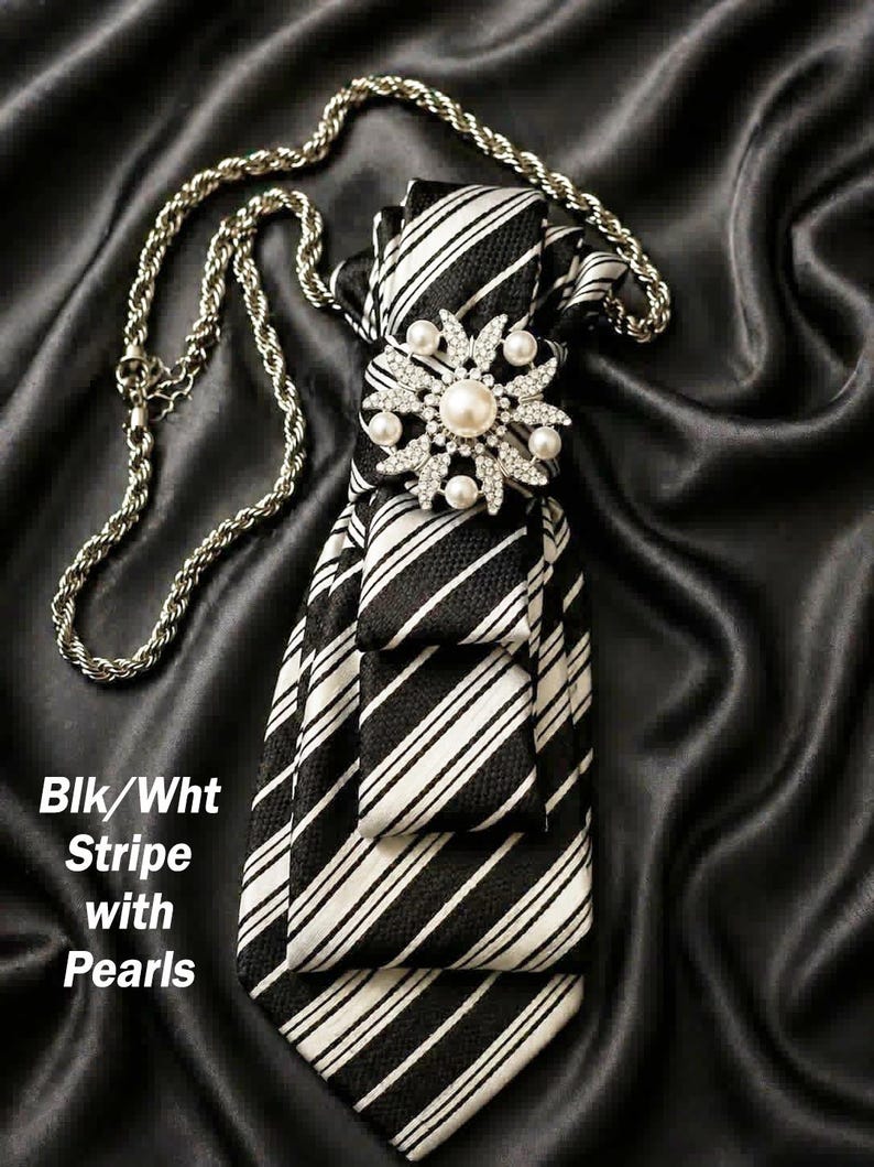 May include: Black and white striped tie with a pearl and rhinestone embellishment. A silver chain is attached to the tie. The text "Blk/Wht Stripe with Pearls" is visible.