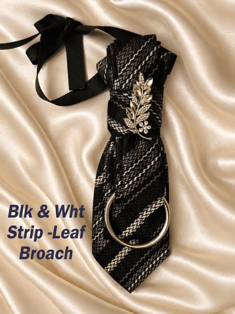 May include: A black and white striped tie with a silver leaf brooch and a silver ring. The tie has a black ribbon and the text "Blk & Wht Strip-Leaf Broach". The tie is displayed on a satin surface.