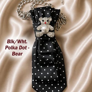 May include: A black and white polka dot tie with a silver chain necklace. The tie features a jeweled teddy bear brooch with a pearl. The text "Blk/Wht. Polka Dot - Bear" is visible.
