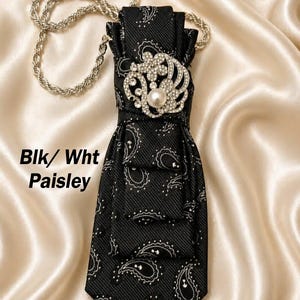 May include: Black and white paisley necktie with a decorative silver chain. The tie features a jeweled brooch with a pearl center. The text "Blk/ Wht Paisley" is visible on the left side.