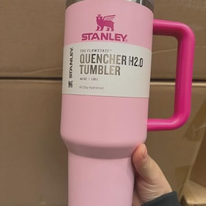 Puede incluir: Un vaso Stanley Quencher H2.0 rosa con asa y tapa a juego. El vaso tiene el logotipo de Stanley y el texto "QUENCHER H2.0 TUMBLER" y "40 OZ | 1,18 L". Dise&ntilde;ado para la hidrataci&oacute;n durante todo el d&iacute;a.