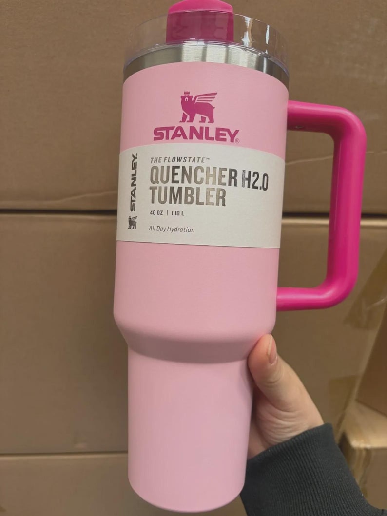 Puede incluir: Un vaso Stanley Quencher H2.0 rosa con asa y tapa a juego. El vaso tiene el logotipo de Stanley y el texto "QUENCHER H2.0 TUMBLER" y "40 OZ | 1,18 L". Dise&ntilde;ado para la hidrataci&oacute;n durante todo el d&iacute;a.