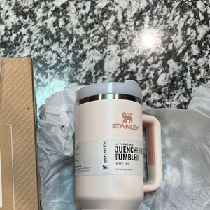 May include: A light pink Stanley Quencher tumbler with a handle and lid. The tumbler has the Stanley logo and the text "QUENCHER TUMBLER" on the side. It is 1.1L and designed for all-day hydration.