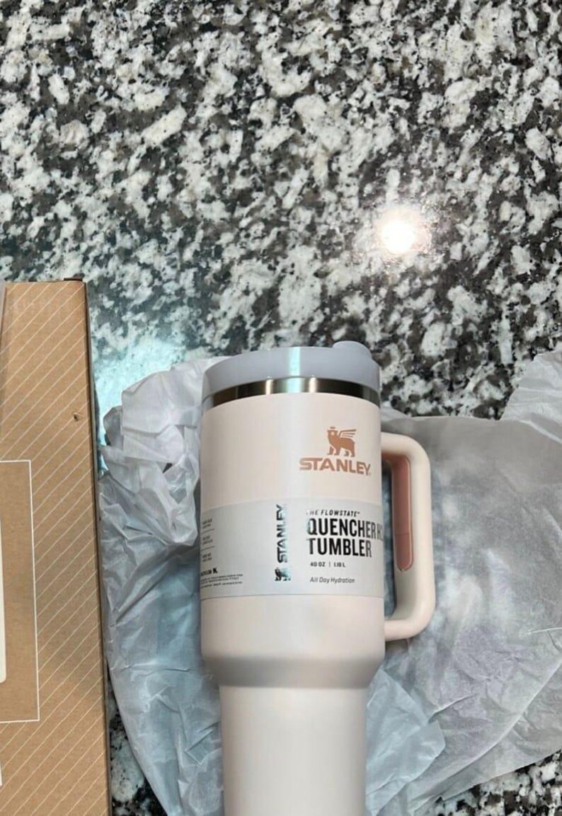 May include: A light pink Stanley Quencher tumbler with a handle and lid. The tumbler has the Stanley logo and the text "QUENCHER TUMBLER" on the side. It is 1.1L and designed for all-day hydration.