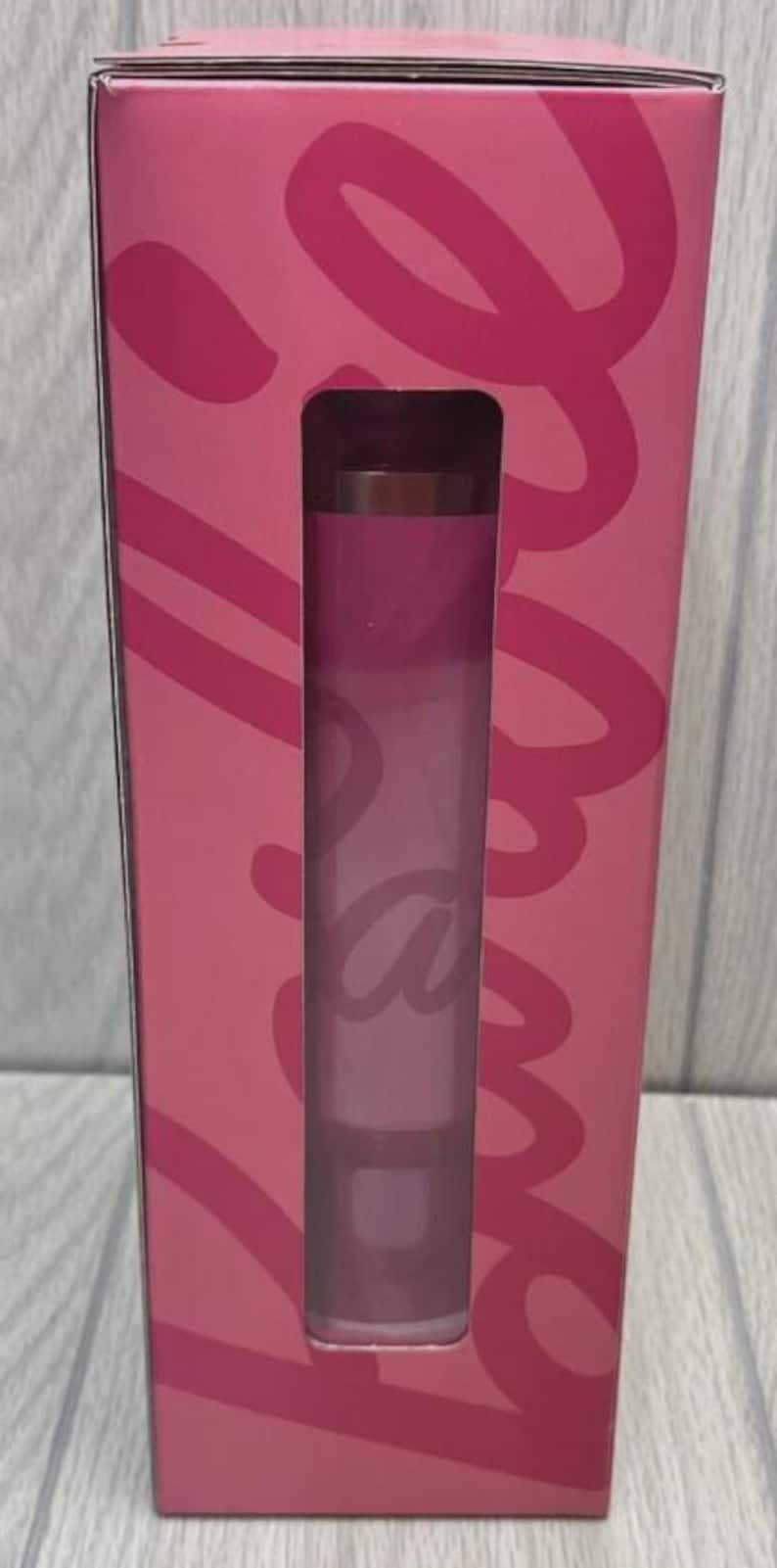 Op de afbeelding: Een roze lipstick tube wordt getoond in een roze doos met een uitgesneden venster. De lipstick heeft een verloop van roze tinten. De doos heeft een cursief ontwerp in een donkerdere roze tint.