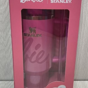 Op de afbeelding: Een roze Barbie- en Stanley-geschenkset. De doos heeft het Barbie-logo en een silhouet van Barbie. Het Stanley-logo is ook zichtbaar. De set bevat een roze beker met het woord "Barbie" erop.