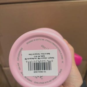Puede incluir: Un vaso rosa de la marca Stanley, 1,18L, con una etiqueta blanca y un c&oacute;digo de barras. La parte inferior del vaso tiene el texto "Designed in Seattle WA" y "Ethically Manufactured in China".