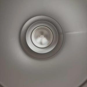 Puede incluir: Primer plano de un objeto circular plateado con anillos conc&eacute;ntricos. El centro tiene un peque&ntilde;o elemento circular reflectante. El objeto parece ser de metal y tiene una superficie lisa y pulida.