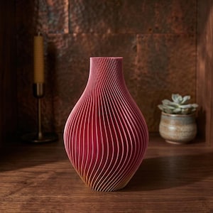 May include: A red and yellow decorative vase with a ribbed design. The vase has a bulbous body and a narrow neck. The vase is made of a material that appears to be wood or paper. The vase is sitting on a wooden surface.