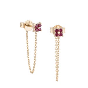 Può includere: Un paio di orecchini color oro con un design floreale. Ogni orecchino presenta un gruppo di pietre preziose rosse al centro del fiore e una delicata catena. Gli orecchini sono su uno sfondo bianco.