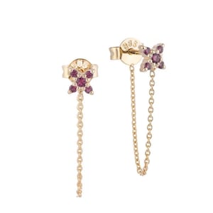 Peut inclure: Une paire de boucles d'oreilles dorées avec un motif floral, chacune ornée de petites pierres précieuses rondes de couleur magenta. Une fine chaîne dorée pend de chaque boucle d'oreille, ajoutant une touche d'élégance. Les boucles d'oreilles sont sur fond blanc.